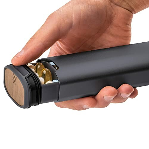 Hand holding a black pill organizer with visible compartments.