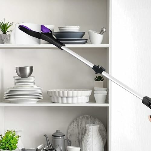 Reaching tool grabbing items on a kitchen shelf.