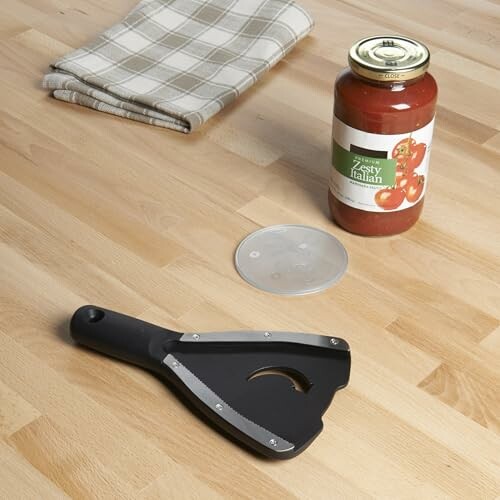 Kitchen tools on a wooden counter including a jar of sauce, a grater, and a cloth