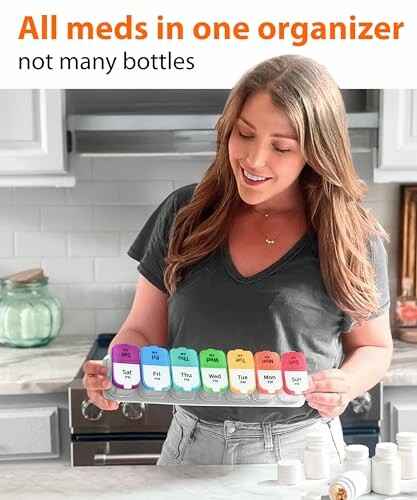 Woman holding a colorful weekly pill organizer in a kitchen setting.